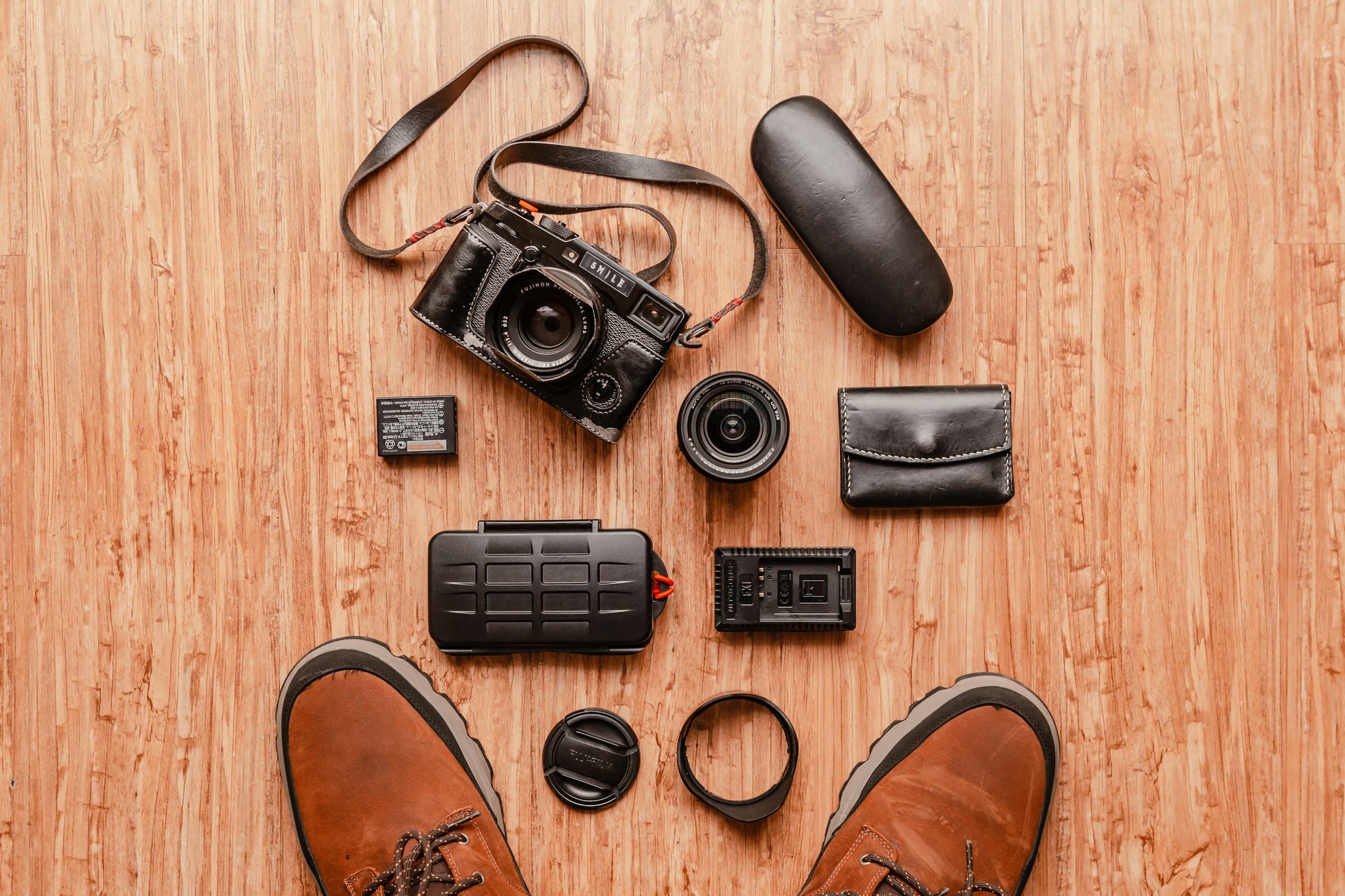 A travel gear flat lay with shoes, camera and other packing essentials on a wooden surface