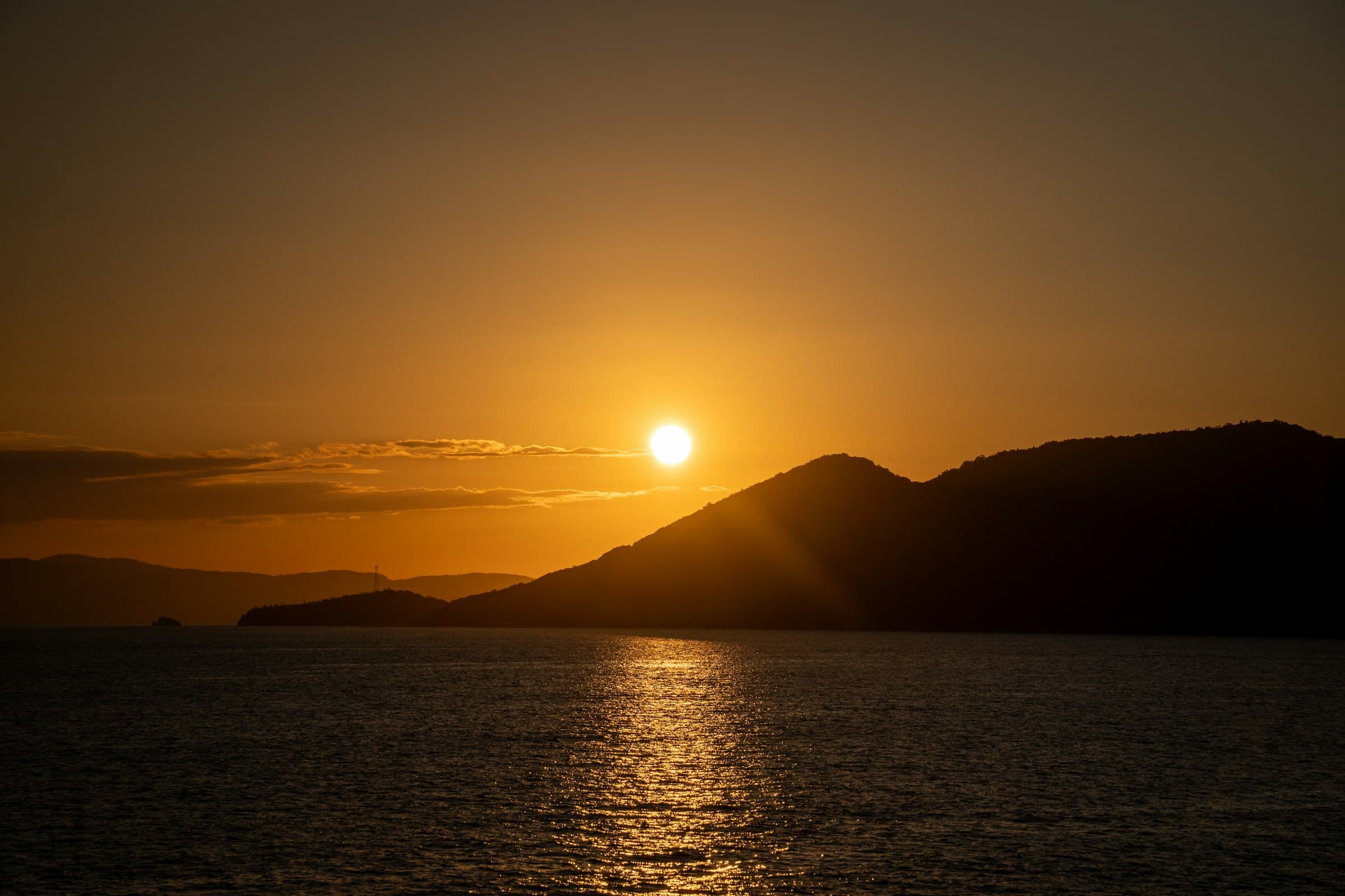 A calm sunset over the ocean with silhouetted mountains on the horizon