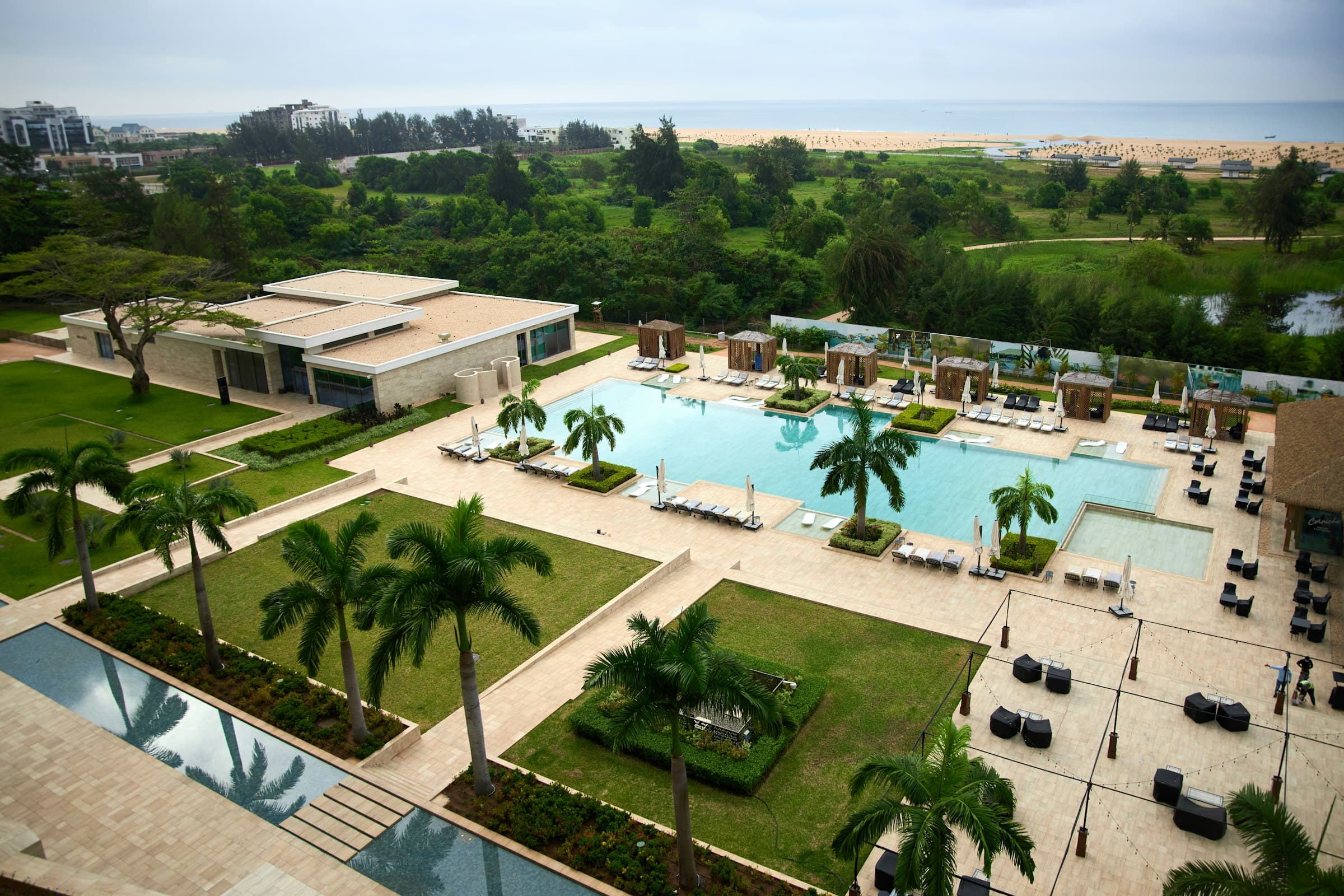 Aerial view of a beach resort complex with a swimming pool, palm trees and green lawns