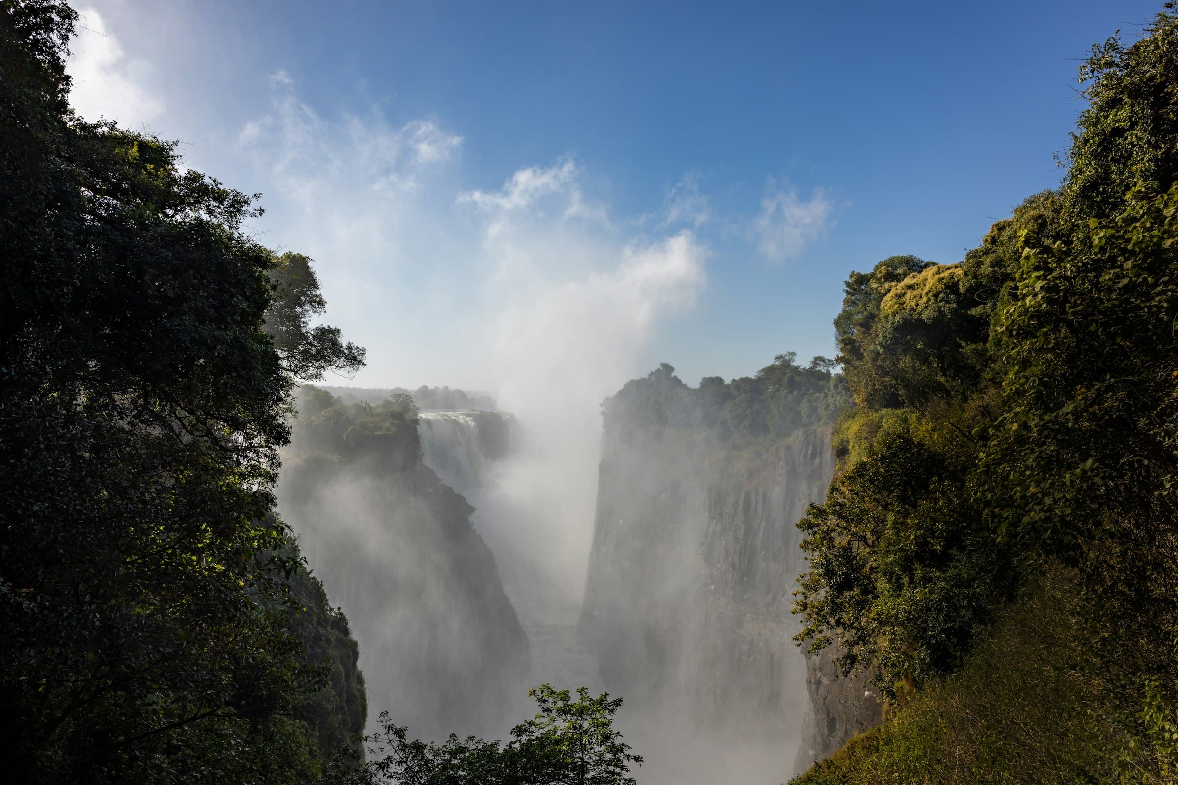 Wide distant view of Victoria Falls with spray rising from the gorge