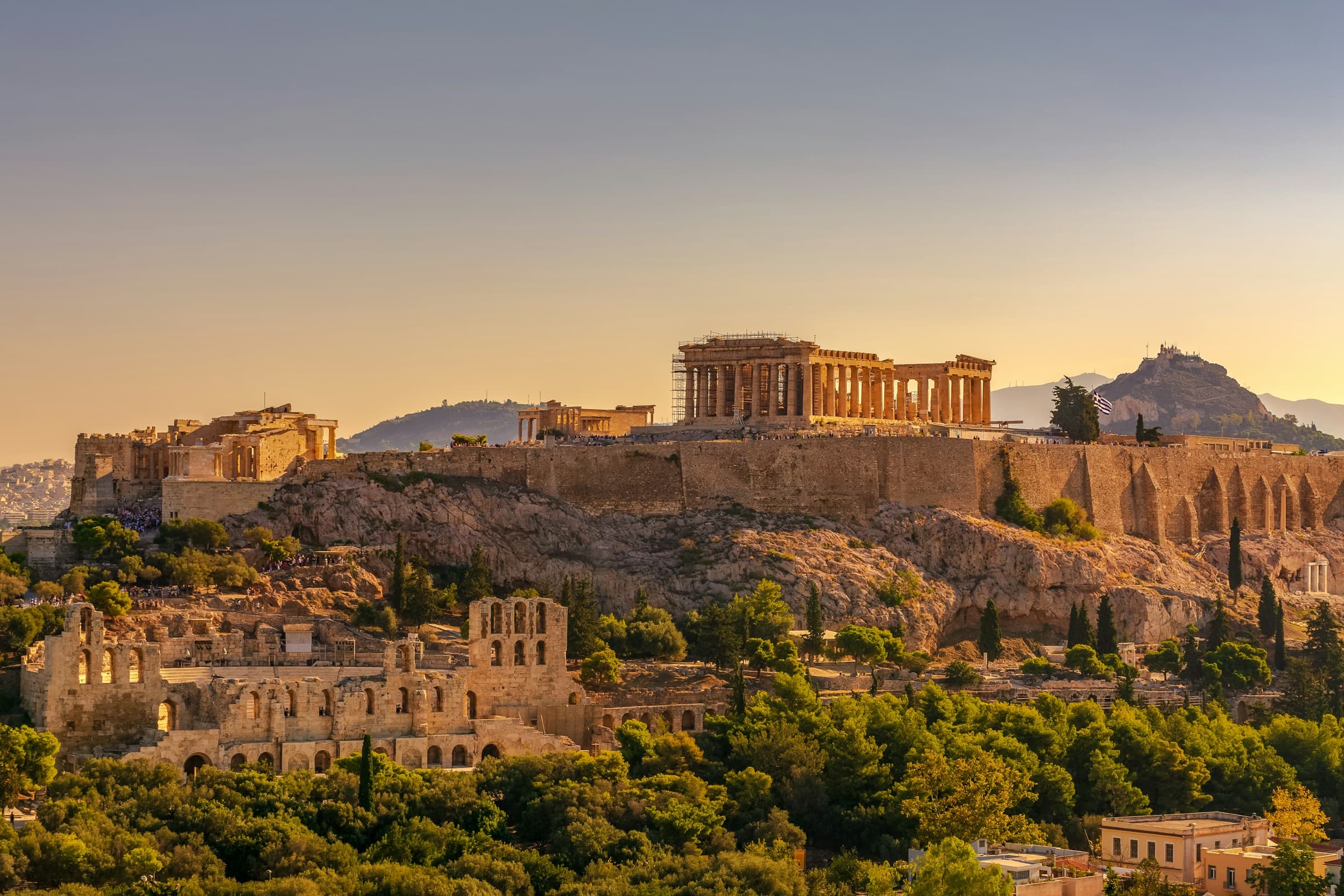 The Acropolis of Athens with the Parthenon and the Odeon of Herodes Atticus in golden evening light, seen from Philopappos Hill, with Lycabettus behind