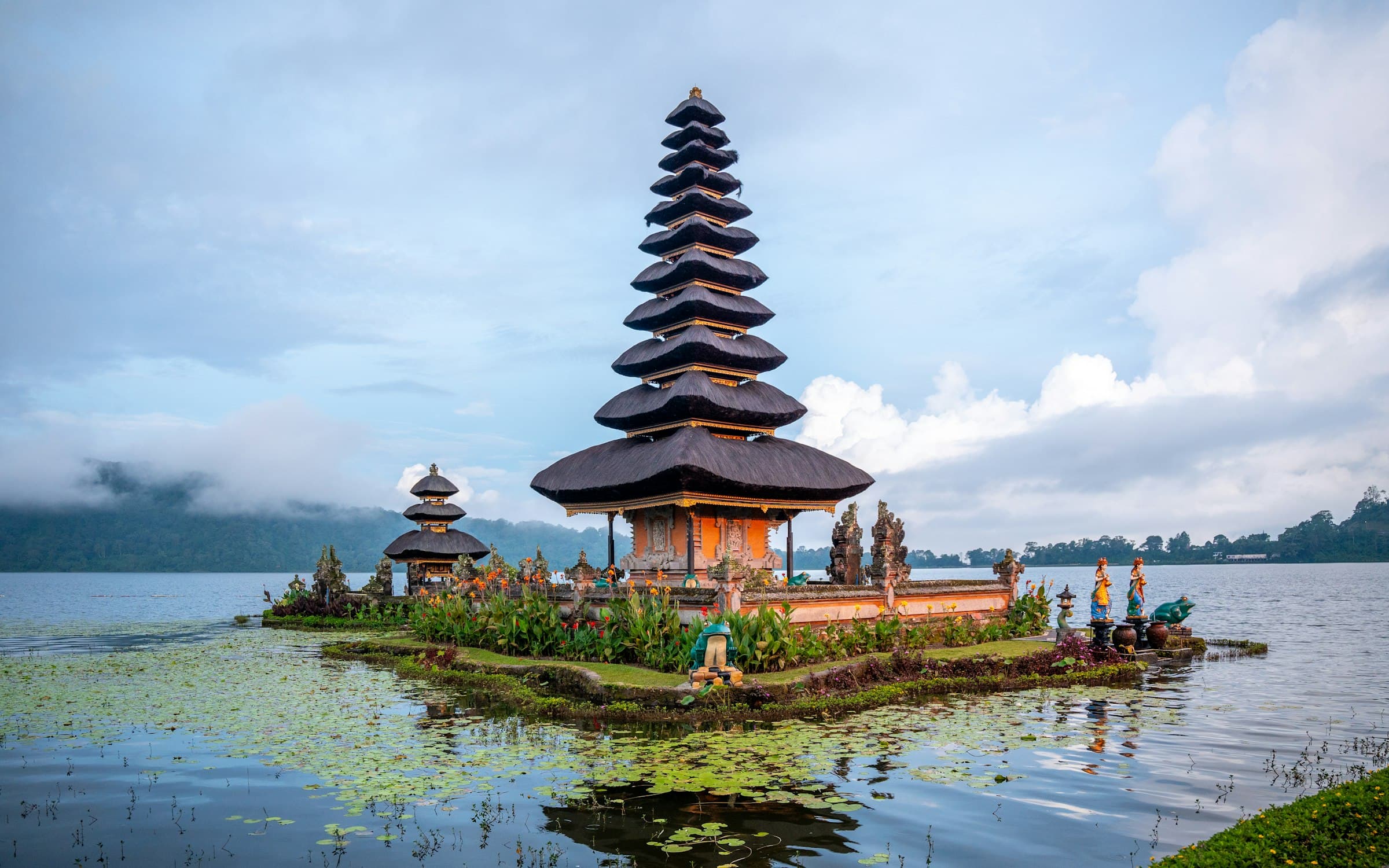The multi-tiered thatched shrine of Pura Ulun Danu Beratan on Lake Beratan in Bali's highlands, reflected in still water with clouds over the hills behind
